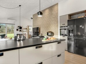 A modern kitchen with a large island, black appliances, and a brick accent wall. - "Muriel" - 1.6km from the sea by Interhome (Blokhus)