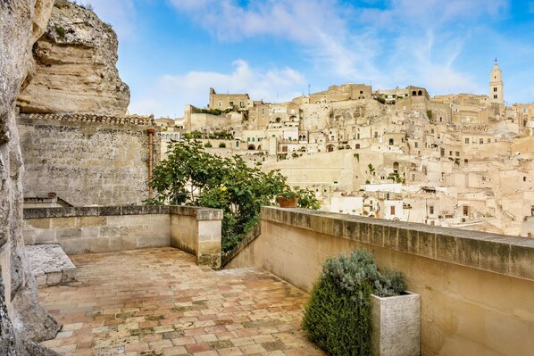 A stone terrace with a view of a historic town with layered buildings and a prominent tower. - La Corte Dei Pastori Luxury (Matera)