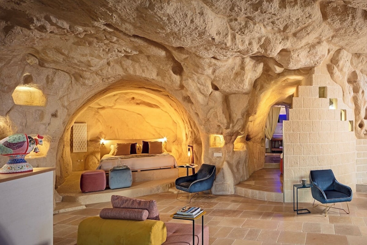 Un interior acogedor, similar a una cueva, con una cama, zona de estar y una escalera que sube a otro nivel.