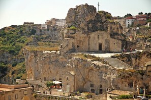 A historic building with a staircase leading to a door, situated on a rocky cliff with a view of the surrounding town. - La Corte Dei Pastori Luxury (Matera)