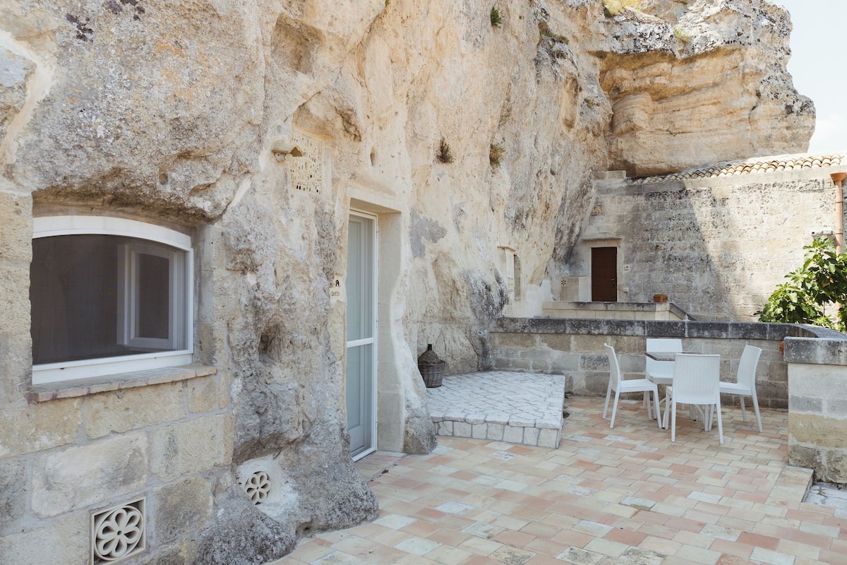 Un edificio de piedra con ventana, puerta y zona de estar al aire libre.