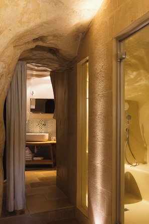 A narrow, stone-walled bathroom with a shower, a sink, and a mirror. - La Corte Dei Pastori Luxury (Matera)
