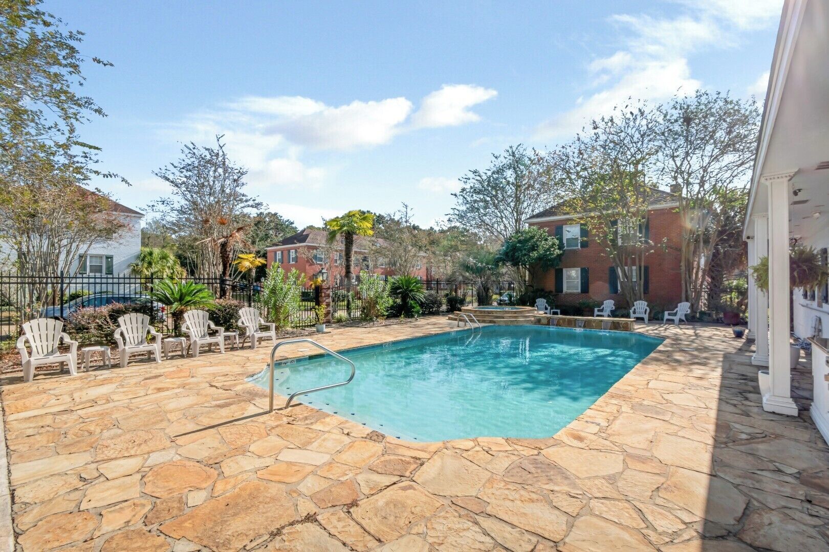 A swimming pool with stone tiles, surrounded by white chairs and a brick building.
