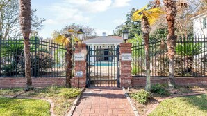 Una entrada tancada amb un camí de maons que condueix a una zona de piscina, envoltada de palmeres i una tanca.