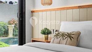 A bedroom with a bed, a bedside table with a plant, a hanging light fixture, and a view of a swimming pool. - Darani Villa by Kozystay - Ungasan (Ungasan)