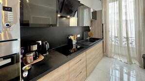 A modern kitchen with stainless steel appliances, a black countertop, wooden cabinets, and a large window with sheer curtains. - Ze Perfect Place - Centre - Durandy - 2 Bdrms - AC (Nice)