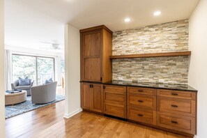 A modern kitchen with wooden cabinets, a stone backsplash, and a black countertop. - New Luxury Waterfront Retreat with Pool, Private Pier & Multiple EnSuite King Bedrooms (Annapolis)