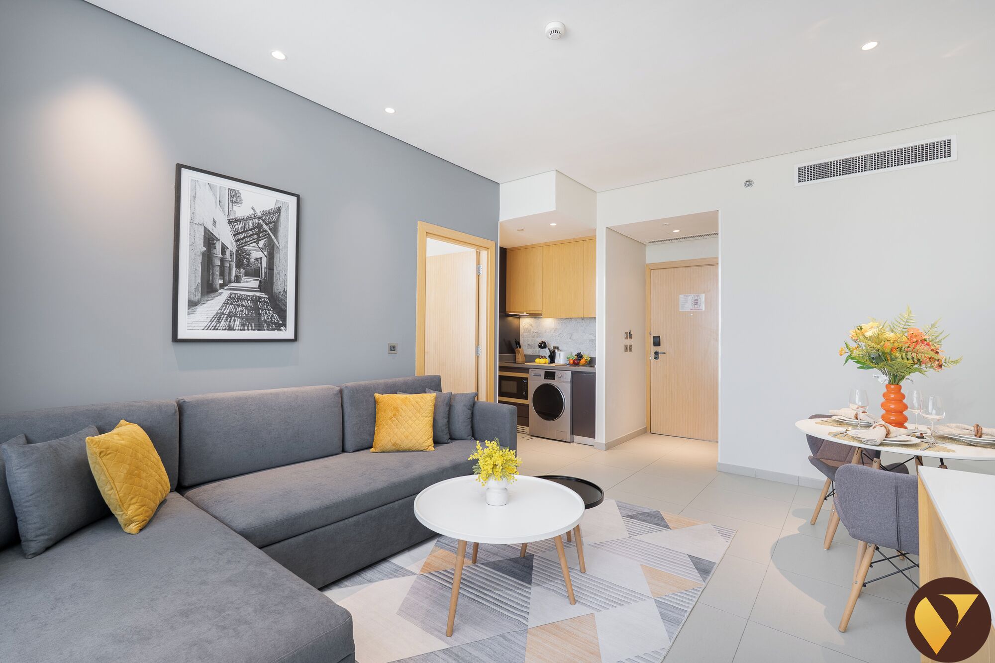 A modern living room with a grey sofa, a white coffee table, and a dining area with a table set for two.