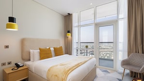 A hotel room with a large bed, a bedside table with a phone, a chair, and a balcony with a city view. - Vogue | JVT near Springs Souk Mall (Dubai)