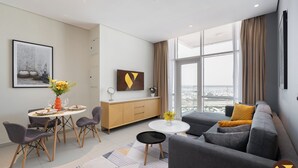 A modern living room with a sofa, a dining table with chairs, a small coffee table, and a large window with a view of the city. - Vogue | JVT near Springs Souk Mall (Dubai)