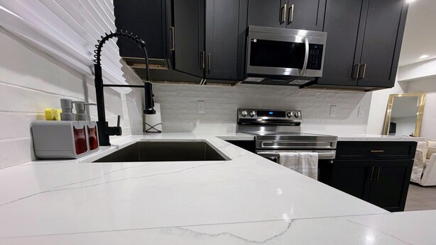 Uma cozinha moderna com armários escuros, eletrodomésticos de aço inoxidável e bancada de mármore branco.