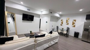 Uma sala de estar moderna com sofá, televisão e área de jantar com cadeiras e mesa.