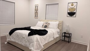 Quarto com cama, mesa de cabeceira, luminária e obras de arte na parede.
