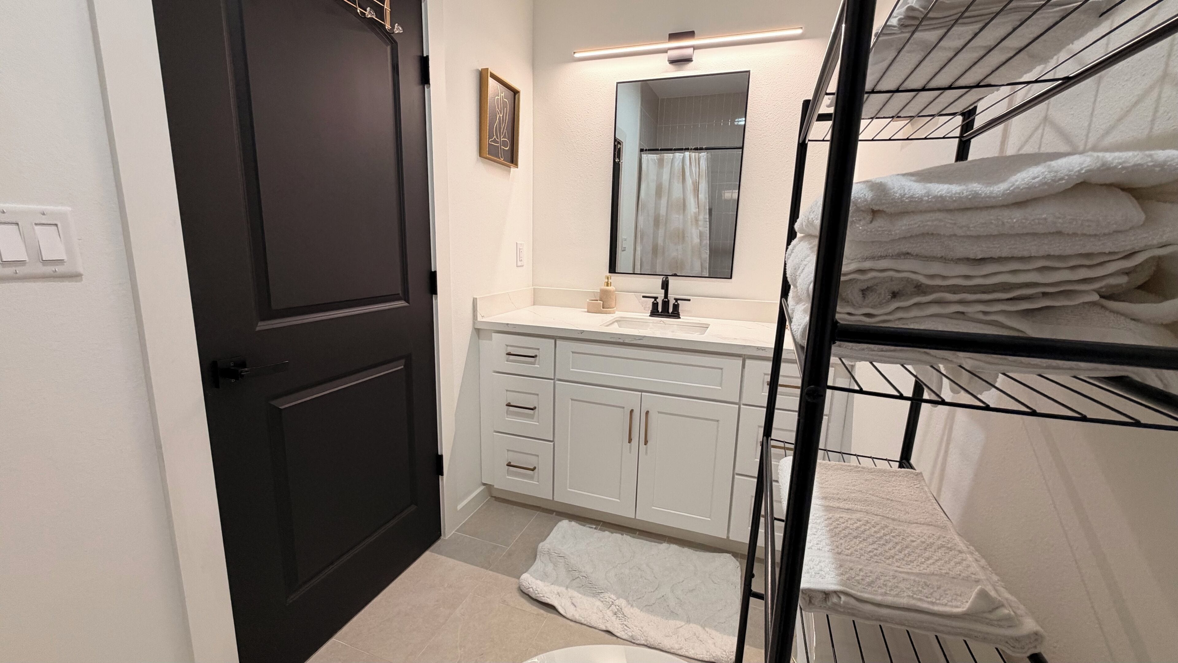 A bathroom with a dark door, white cabinets, a sink, a mirror, and a towel rack.