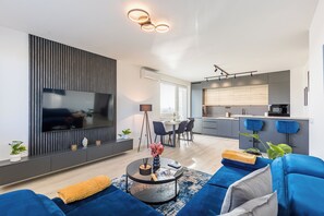 Un salon moderne avec un grand téléviseur à écran plat, une table basse ronde et des canapés bleus.