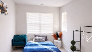 A bedroom with a bed, a chair, a nightstand, a window, and a wall-mounted rack. - Luxury 3BR 3.5BA Townhome Near Uptown & Stadium (Charlotte)