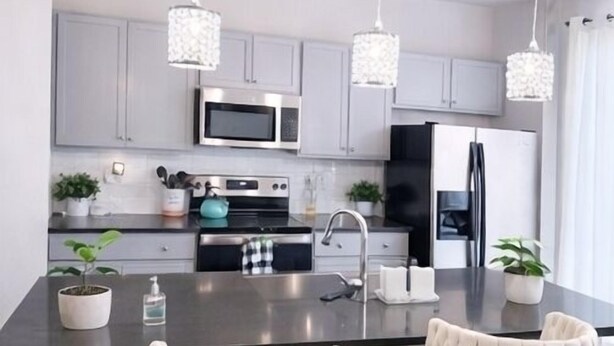 A modern kitchen with grey cabinets, stainless steel appliances, and a central island with bar stools. - Luxury 3BR 3.5BA Townhome Near Uptown & Stadium (Charlotte)