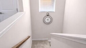 A narrow staircase with a carpeted floor, white walls, a white door, and a window with blinds. - Luxury 3BR 3.5BA Townhome Near Uptown & Stadium (Charlotte)