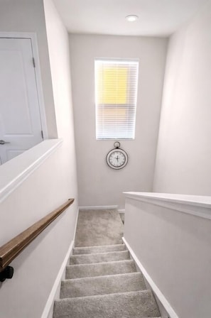 Eine enge Treppe mit Teppichboden, weißen Wänden, einer weißen Tür und einem Fenster mit Jalousien.
