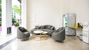 A modern living room with a grey sofa, two armchairs, a small round table, and a coffee machine. - The Shilla Hotel - 신라호텔 (Ho Chi Minh City)