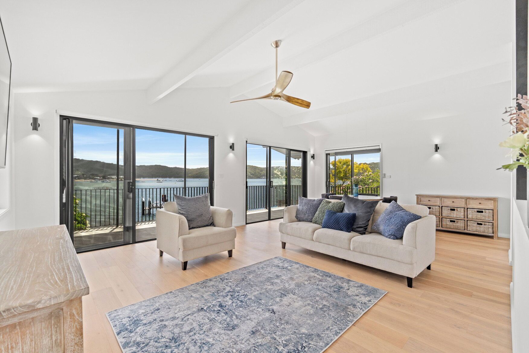 A spacious living room with a large sofa, a smaller armchair, a blue patterned rug, and a ceiling fan.