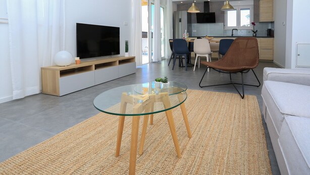 A modern living room with a glass coffee table, a flat-screen TV, a sofa, and a dining area in the background. - Villa Lumaka Sun by Villas Guide (Sibenik)