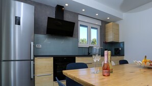 A modern kitchen with stainless steel appliances, a flat-screen TV, and a dining area with a wooden table and chairs. - Villa Lumaka Sun by Villas Guide (Sibenik)