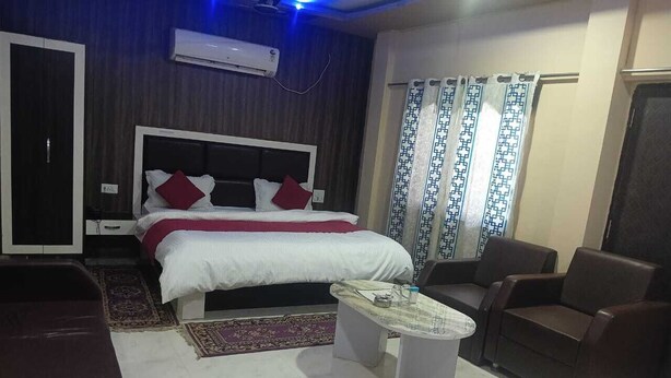 A modern bedroom with a large bed, a coffee table, two armchairs, and a wardrobe. - The Bhuwan Heights Inn (Satna)