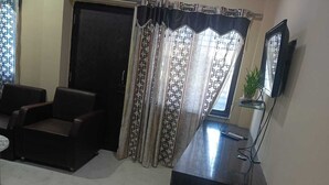 A room with a dark wooden desk, two leather chairs, a television, and patterned curtains. - The Bhuwan Heights Inn (Satna)