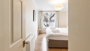 Un dormitorio con cama, ventana con cortinas, radiador y puerta.