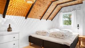 A bedroom with a sloped ceiling, a bed with white bedding, a bedside table, a lamp, and a window with curtains. - 2 bedroom pet friendly home in Thisted (Thisted)