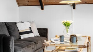 A cozy living room with a dark grey sofa, a white and black patterned throw pillow, a glass coffee table with books and decorative items, a vase with white flowers, and a hanging light fixture. - 2 bedroom pet friendly home in Thisted (Thisted)