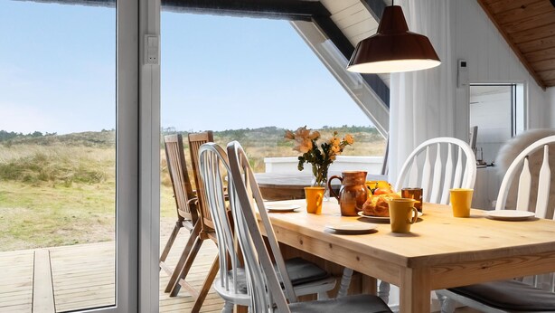 An open-plan dining area with a wooden table, chairs, and a pendant light. A window offers a view of the outdoors. - 2 bedroom pet friendly home in Thisted (Thisted)