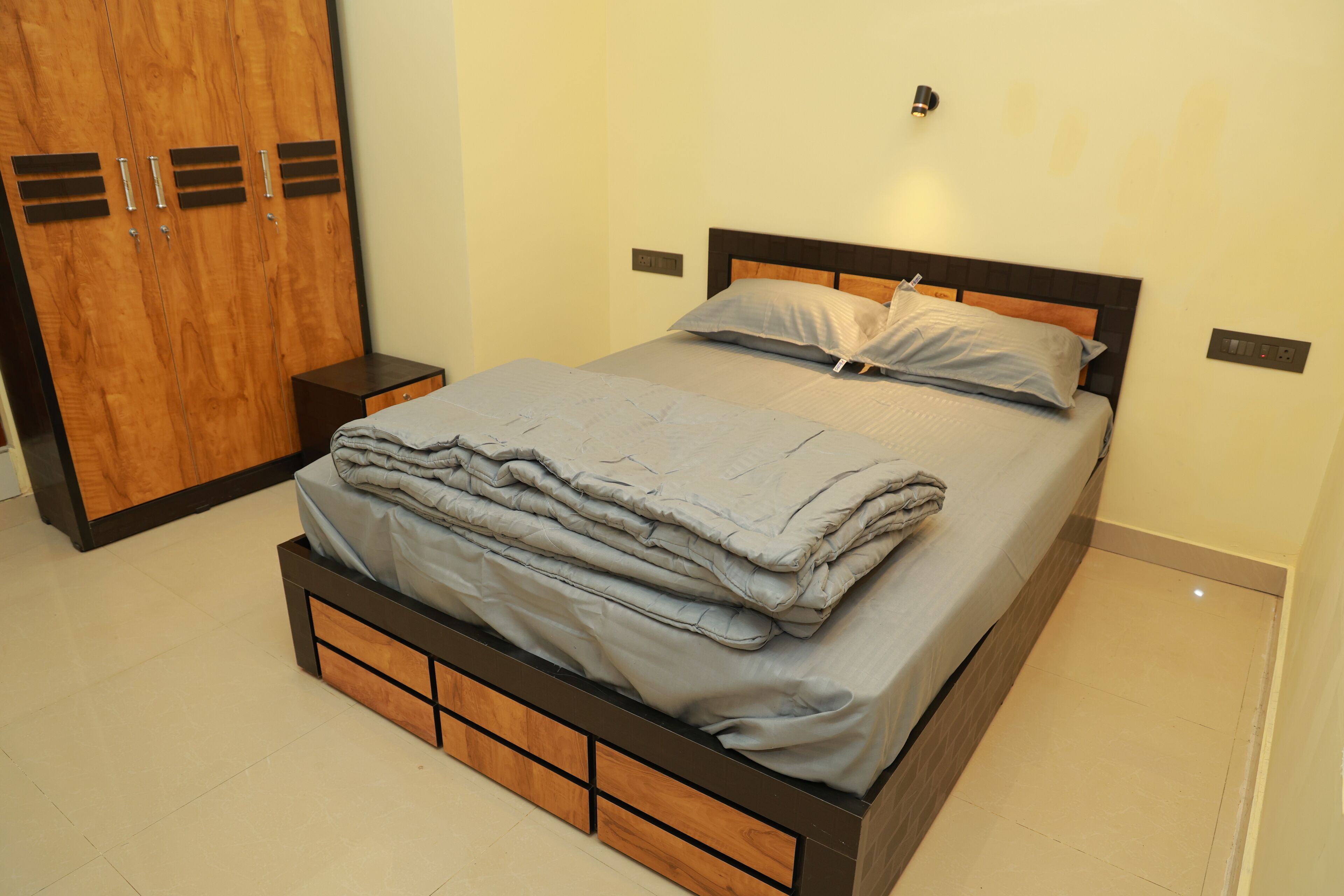 Ein ordentlich bezogenes Bett mit grauer Decke, einem Holzkopfschild und einem Nachttisch mit Lampe.