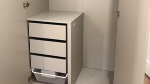 Un vestidor con un aparador blanco, una barra para colgar ropa y una cesta de almacenamiento de malla.