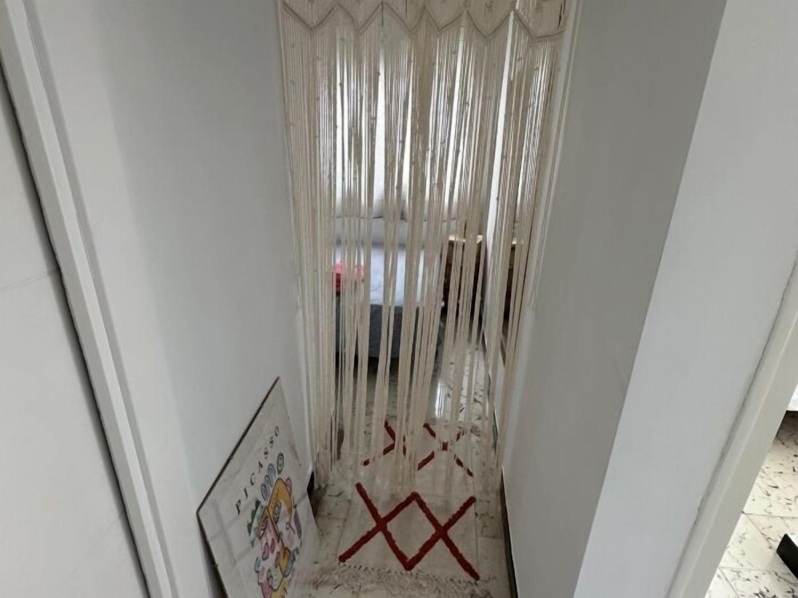 Un pasillo estrecho con una puerta blanca a la izquierda y una 'X' roja marcada en el suelo.