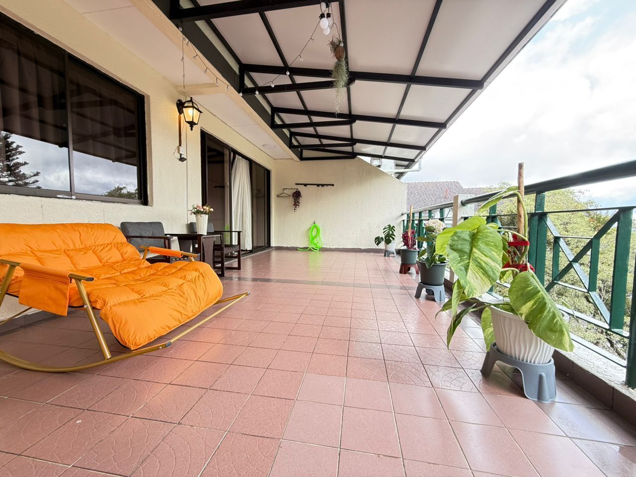 Ein überdachter Balkon mit einem Schaukelstuhl, Topfpflanzen und Blick ins Freie.