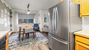 Ett kompakt kök med ett kylskåp i rostfritt stål, träskåp, ett matbord med stolar och ett stort fönster som ger en fin utsikt.