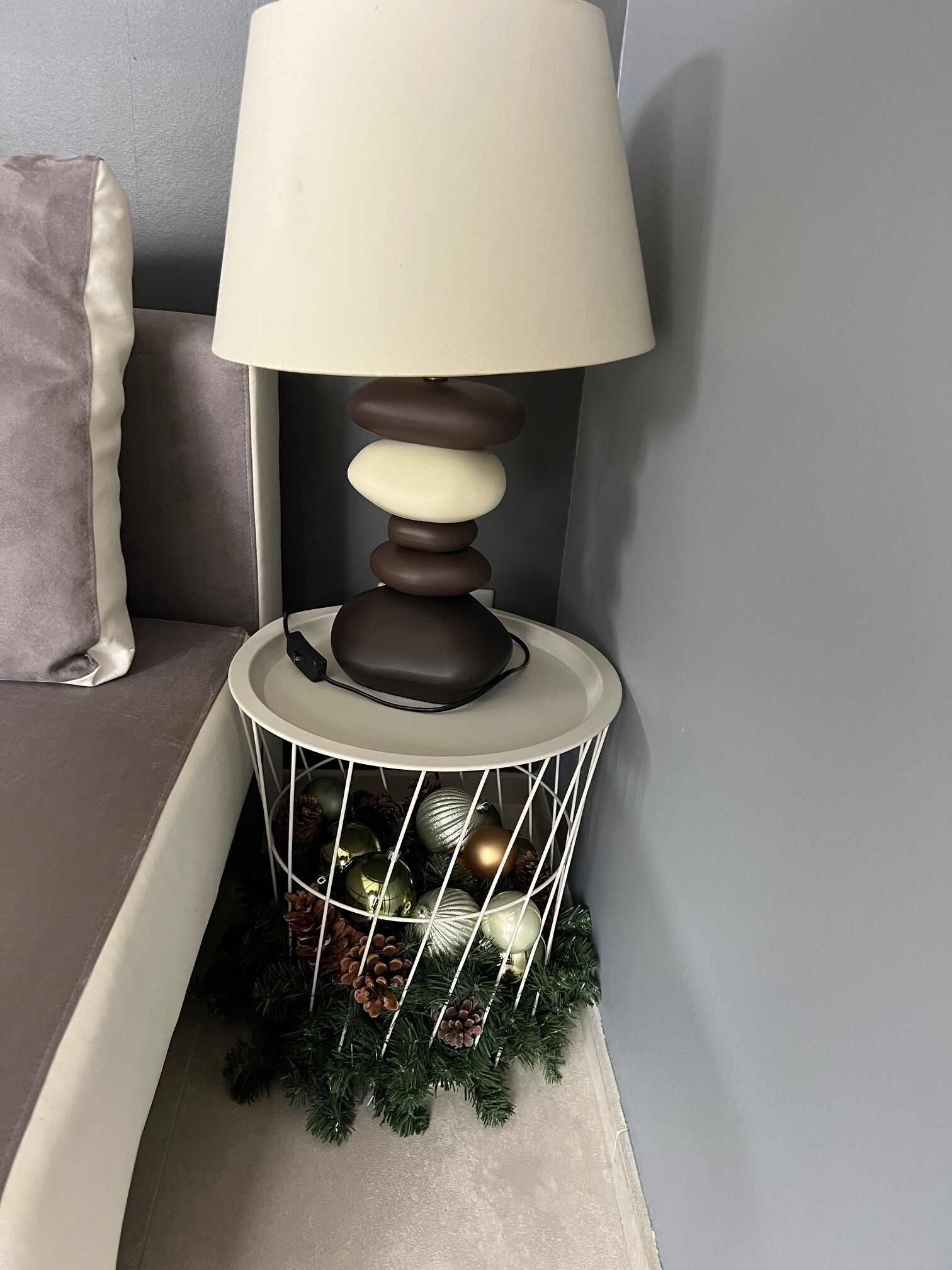 Een hoek met een lamp op een witte standaard, een grijze bank en een witte kussen.