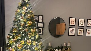 A Christmas tree with gold ornaments and lights, a black shelf with books and a candle, and framed artwork on the wall. - Guest house near EUROPA PARK (Friesenheim)