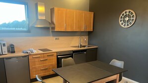 A modern kitchen with wooden cabinets, a built-in oven, a sink, and a dining table with chairs. - Guest house near EUROPA PARK (Friesenheim)
