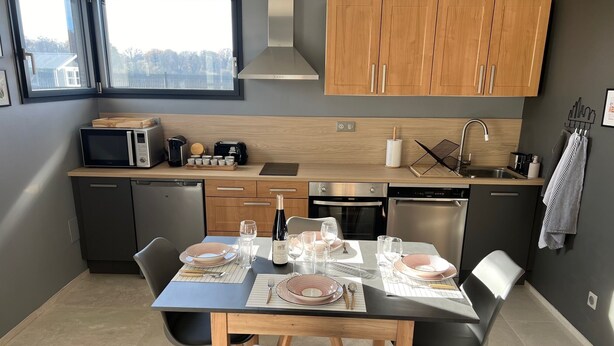 A modern kitchen with wooden cabinets, a built-in microwave, and a dining area set for four. - Guest house near EUROPA PARK (Friesenheim)