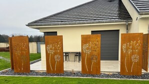 A modern house with a sloped roof, a covered patio, and decorative metal panels with dandelion designs. - Guest house near EUROPA PARK (Friesenheim)