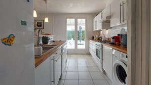 Una cuina moderna amb armaris blancs, taulell de fusta, forn integrat i rentadora.