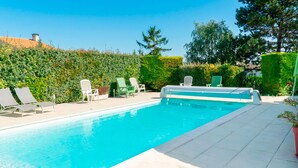 Una piscina rectangular amb una terrassa enrajolada, envoltada de tanques i arbres verds.