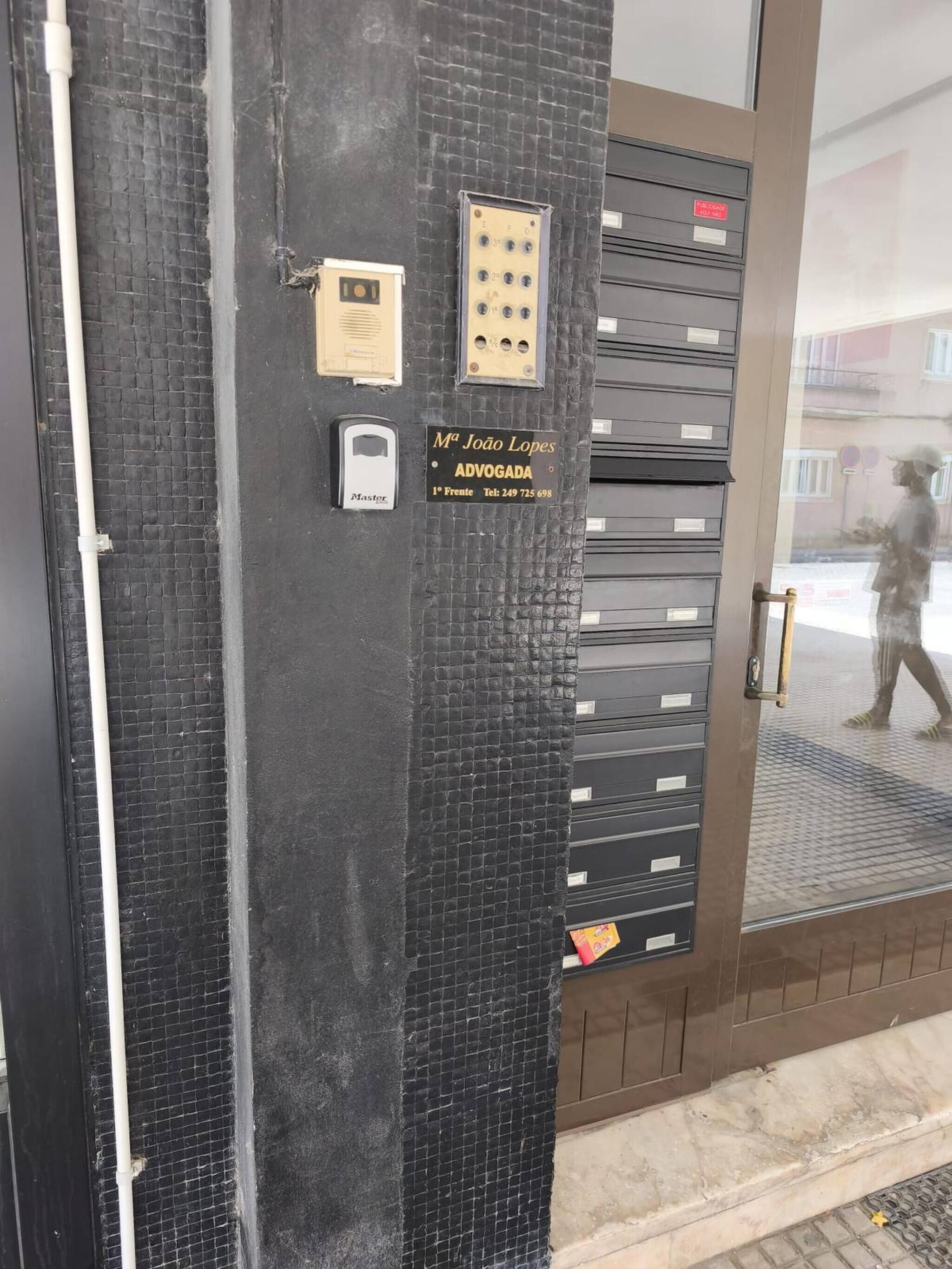 Une porte dotée d’un clavier à code, d’une clé principale et d’une plaque indiquant : « Mª João Lopes, avocate, 1er étage, tél. : 249 725 698 ».