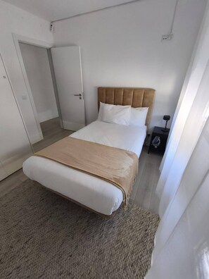 Ein ordentlich eingerichtetes Hotelzimmer mit Bett, Nachttisch und Tür.
