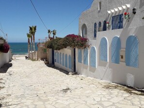 A narrow cobblestone street with white buildings, blue windows, and a view of the sea. - "Gartengeschoss" by Interhome (Chott Mariem)
