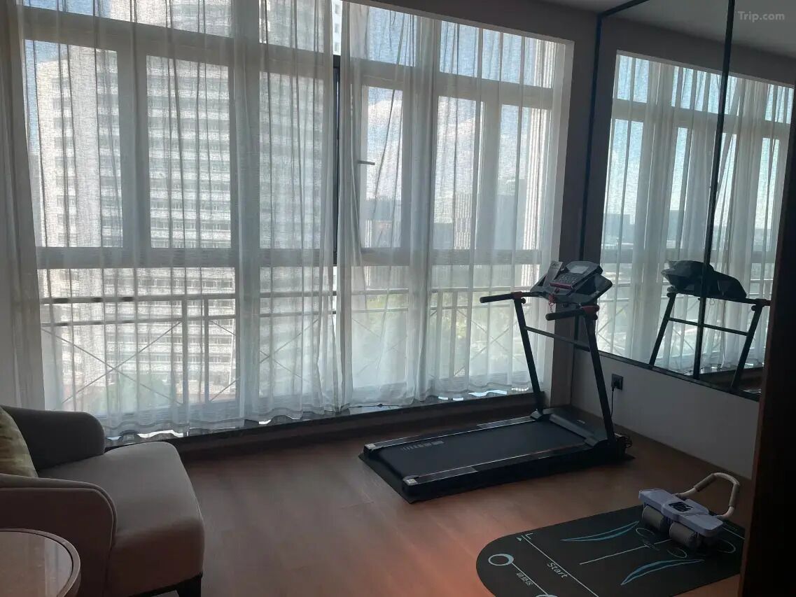A room with a treadmill, a sofa, and large windows with sheer curtains.