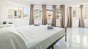 Habitació d'hotel amb un llit, una taula petita i vista a edificis a través de grans finestres.
